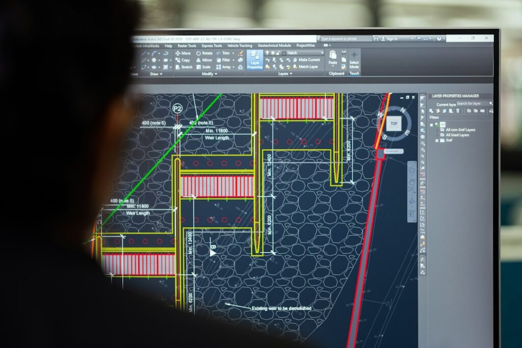 Mechanical engineer reviewing piping plans beside pumps, valves, tanks, and industrial process equipment.